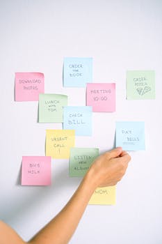 A hand arranging colorful sticky notes with tasks on a white wall.