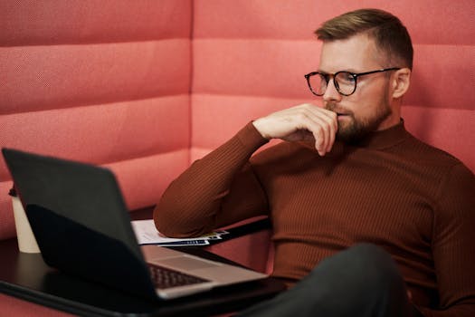 Concentrated businessman wearing eyeglasses working on a laptop indoors.