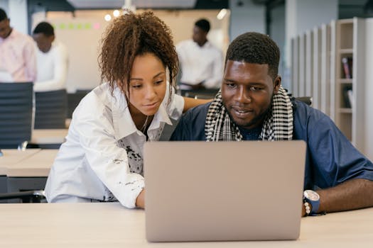 Two colleagues working together on a laptop in a contemporary office environment.