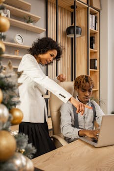 Two professionals collaborate in a modern office setting, focusing on a laptop screen.